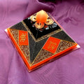 Small Neon Red Cheops Pyramid by Orgone Art Yvonne – low black pyramid with neon orange-red diamond panels bearing gold knot and lotus symbols, a copper filigree crown and orange sphere at the apex