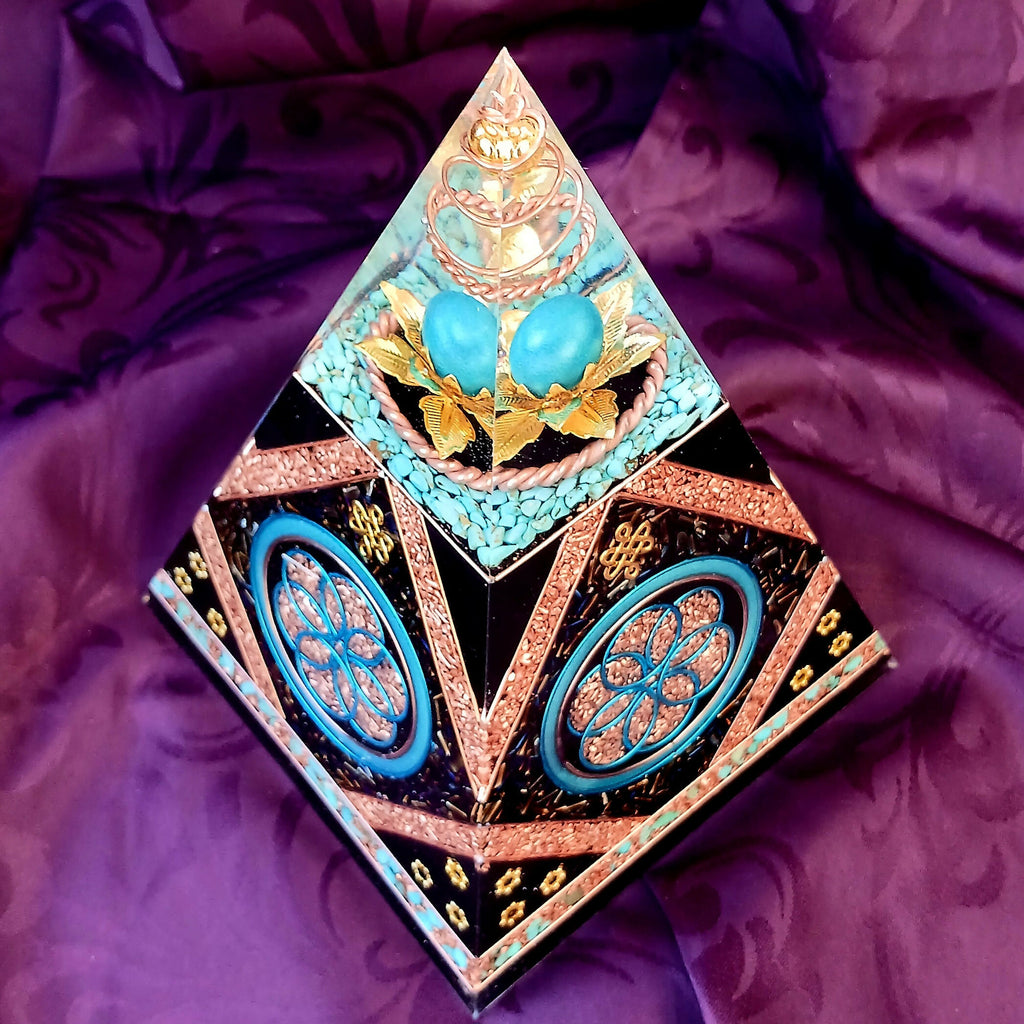 Angled view of Nubian orgonite pyramid showing two Seed of Life panels and blue stones beneath the clear apex.