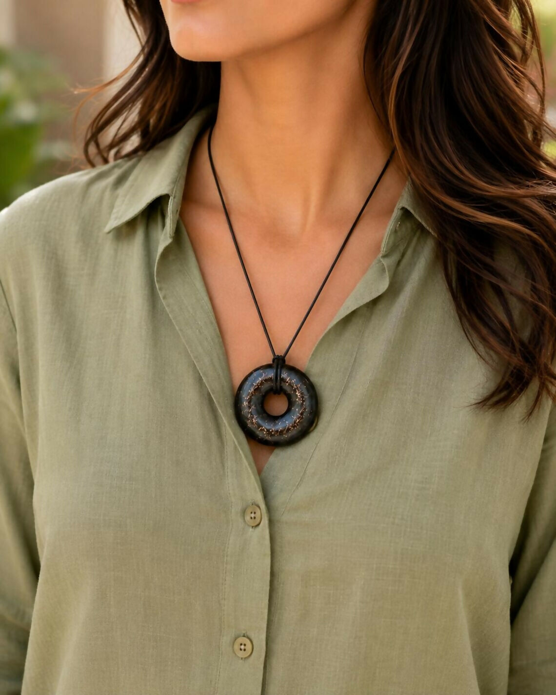The black donut pendant worn on a black cord with an olive-green shirt
