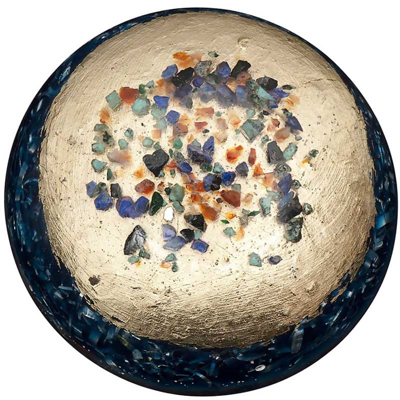 Top view of St. Buster’s Button, showing a rounded dark blue edge, a gold-coloured centre and multicoloured stone pieces