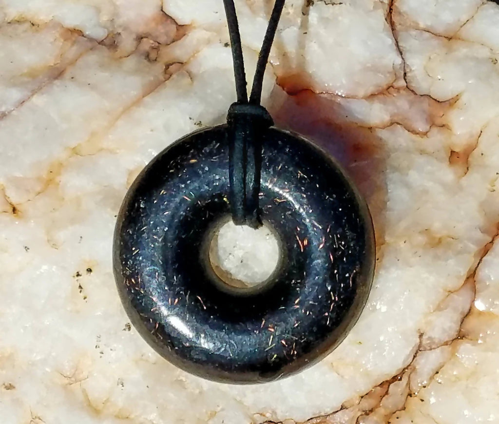 Black Sun Orgonite Donut Pendant by Orgonite Andy – black donut pendant with fine copper flecks on a black cord, on white veined stone