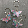 Three butterfly keychains with pink, blue and green swirled colours on silver key rings