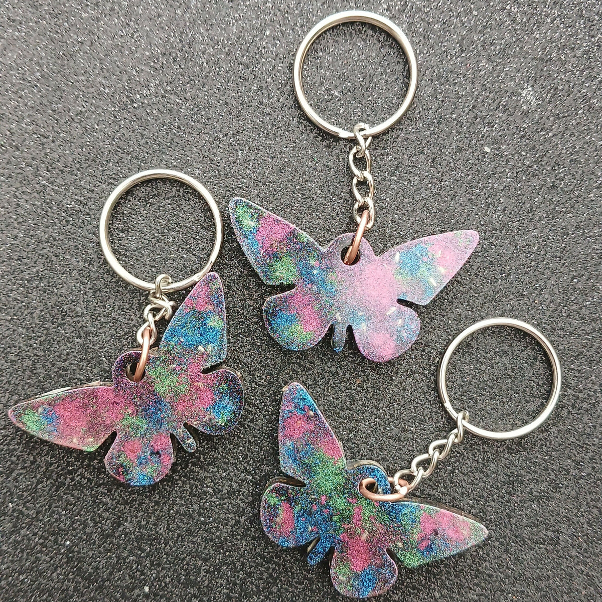 Three butterfly keychains with pink, blue and green swirled colours on silver key rings