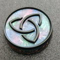 Close view of a round disc with a black raised triquetra knot over shimmering pastel blue and pink