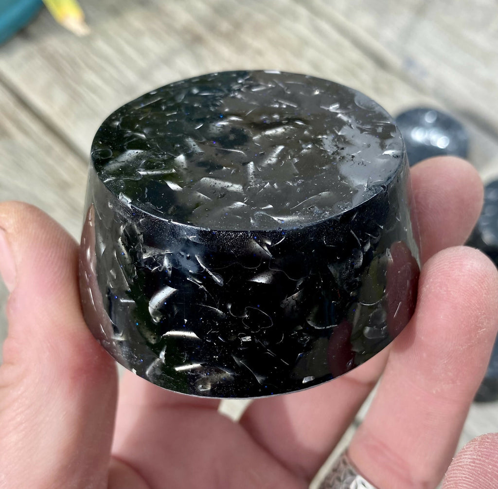 Close-up of one black shungite orgonite towerbuster held in a hand, showing silver flecks through the resin