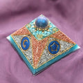 Small Blue Cheops Pyramid by Orgone Art Yvonne – pyramid with a dark blue sphere at the top over turquoise chips, copper-coloured flakes, silver pieces and blue discs with gold symbols