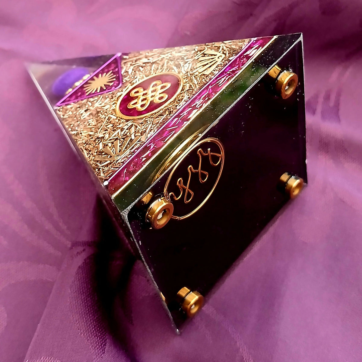 Pyramid on its side showing a dark base with gold feet and a red disc with gold script