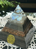 Chinese Dragon Orgonite Pyramid by Gaia's Orgonite – black pyramid with a small silver dragon figure among pale blue stones at the top, a copper shavings band and a gold Flower of Life emblem on the front