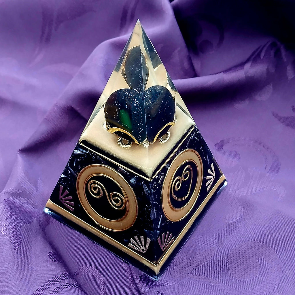 Corner view showing gold double-spiral discs on two faces and the dark glittery heart at the top