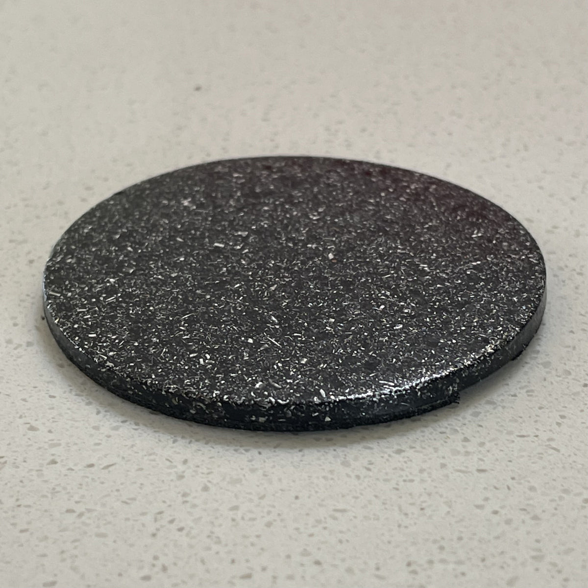 Angled view of a thin dark Maxishield disc with a flecked surface and rounded edge