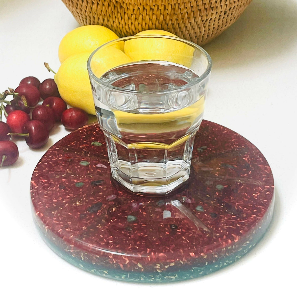 Plate in use under a glass of water, beside cherries, lemons and a woven basket