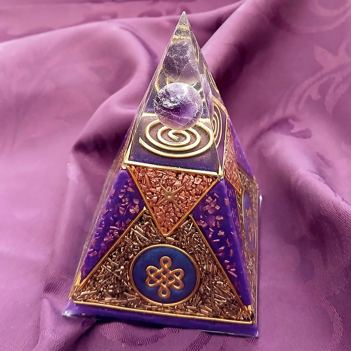 Angled side view showing a gold knot emblem on a blue disc and copper-coloured flake panels between purple triangles