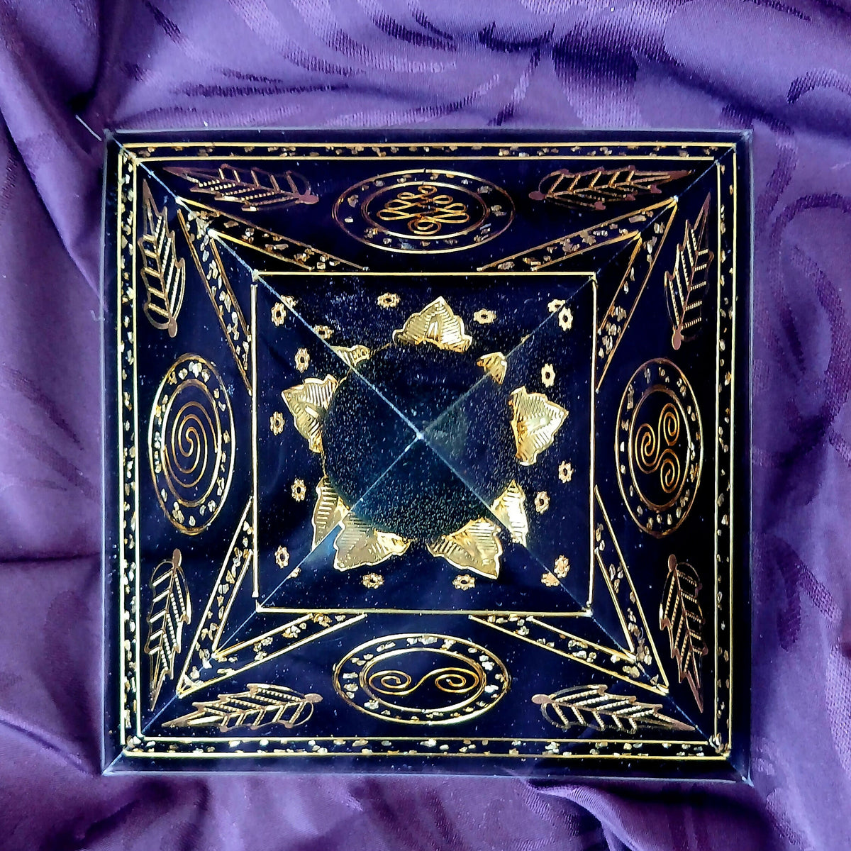 Top-down view of the pyramid with gold spirals and leaf motifs on each face and gold triangles around a clear apex