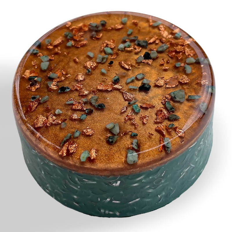 Copper Buster by Orgonise Africa – round puck shape with a copper-coloured top scattered with green stone chips and copper flakes and a dark green patterned side