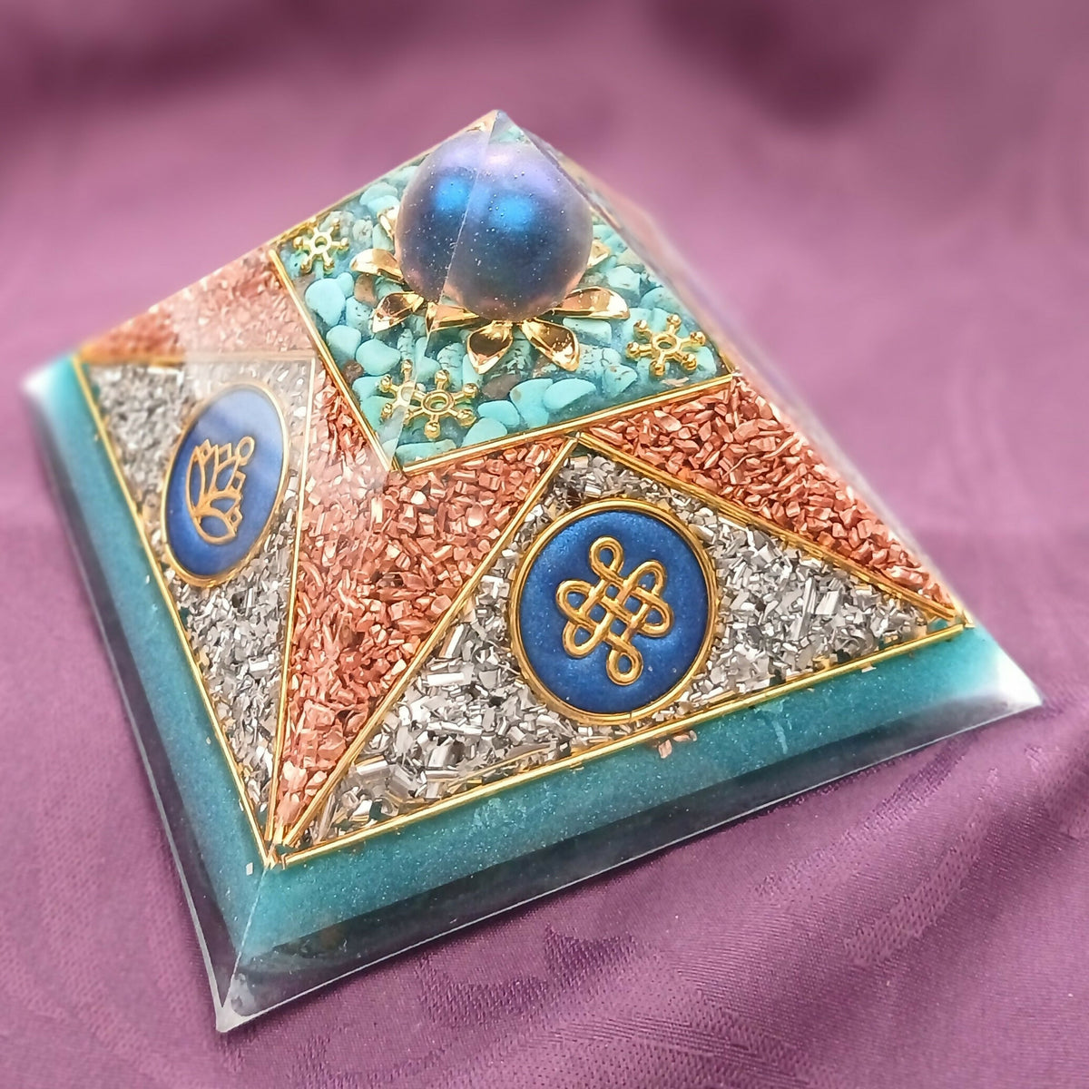 Corner view showing blue discs with a gold endless knot and a gold hand symbol among copper flakes