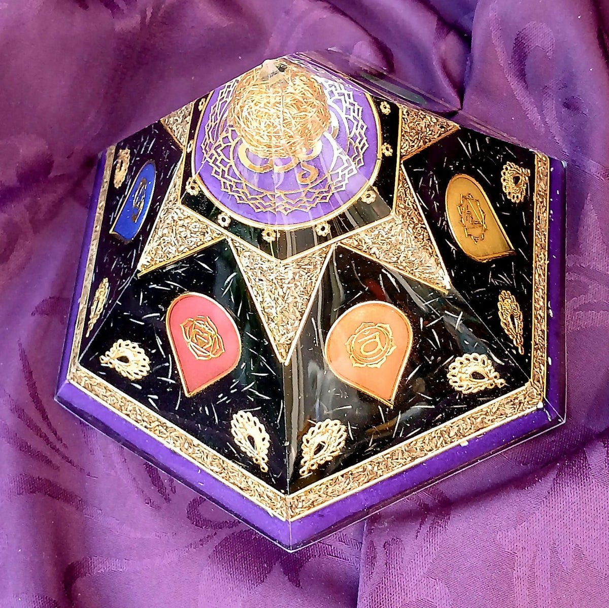 Angled view of chakra orgonite pyramid showing red and orange symbols beneath a purple top panel.