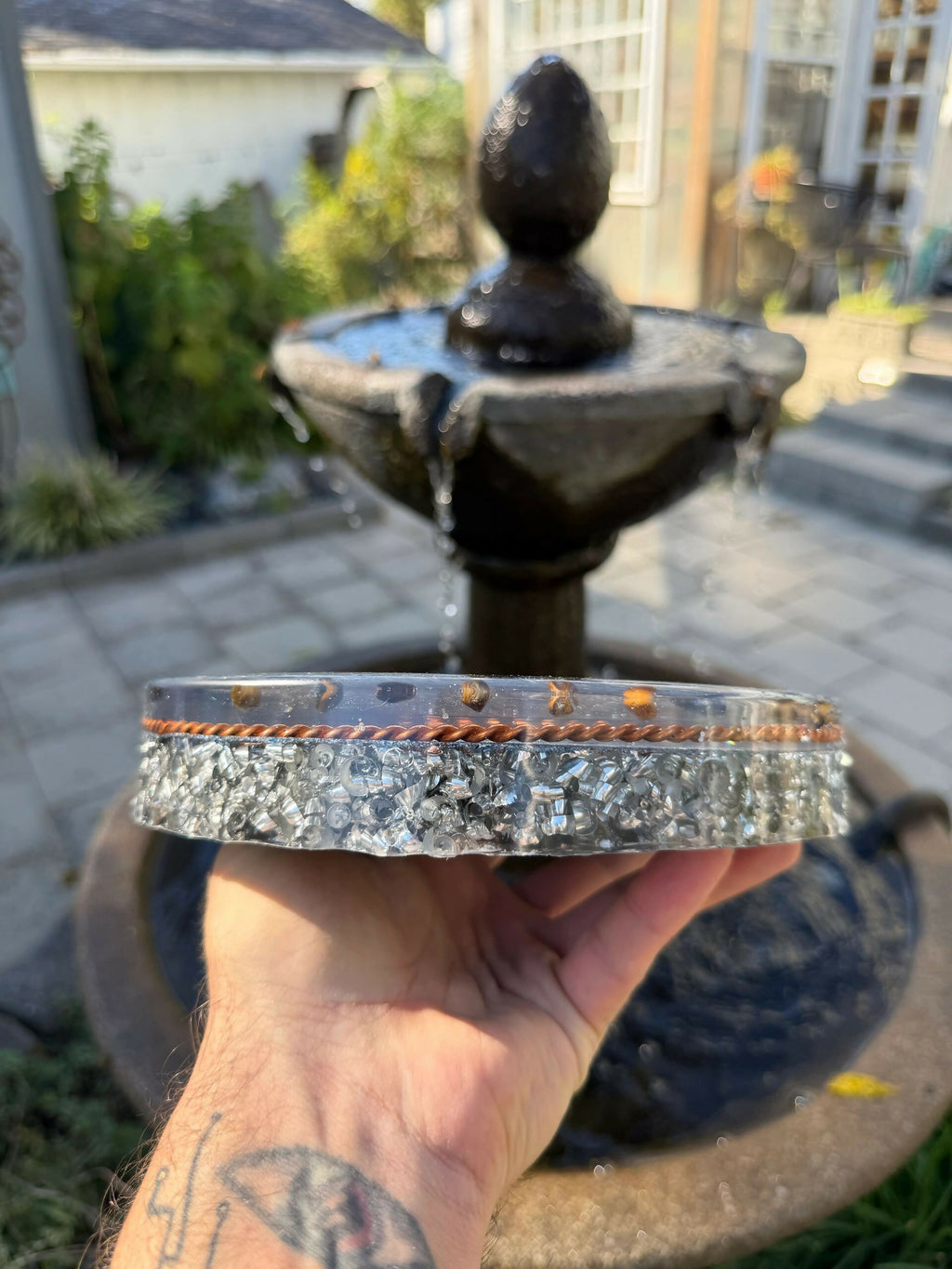 Sri Yantra Charging Plate by Mark Ethan Designs – side view of the round plate held in a hand outdoors, showing its metal-shaving layer and copper rim