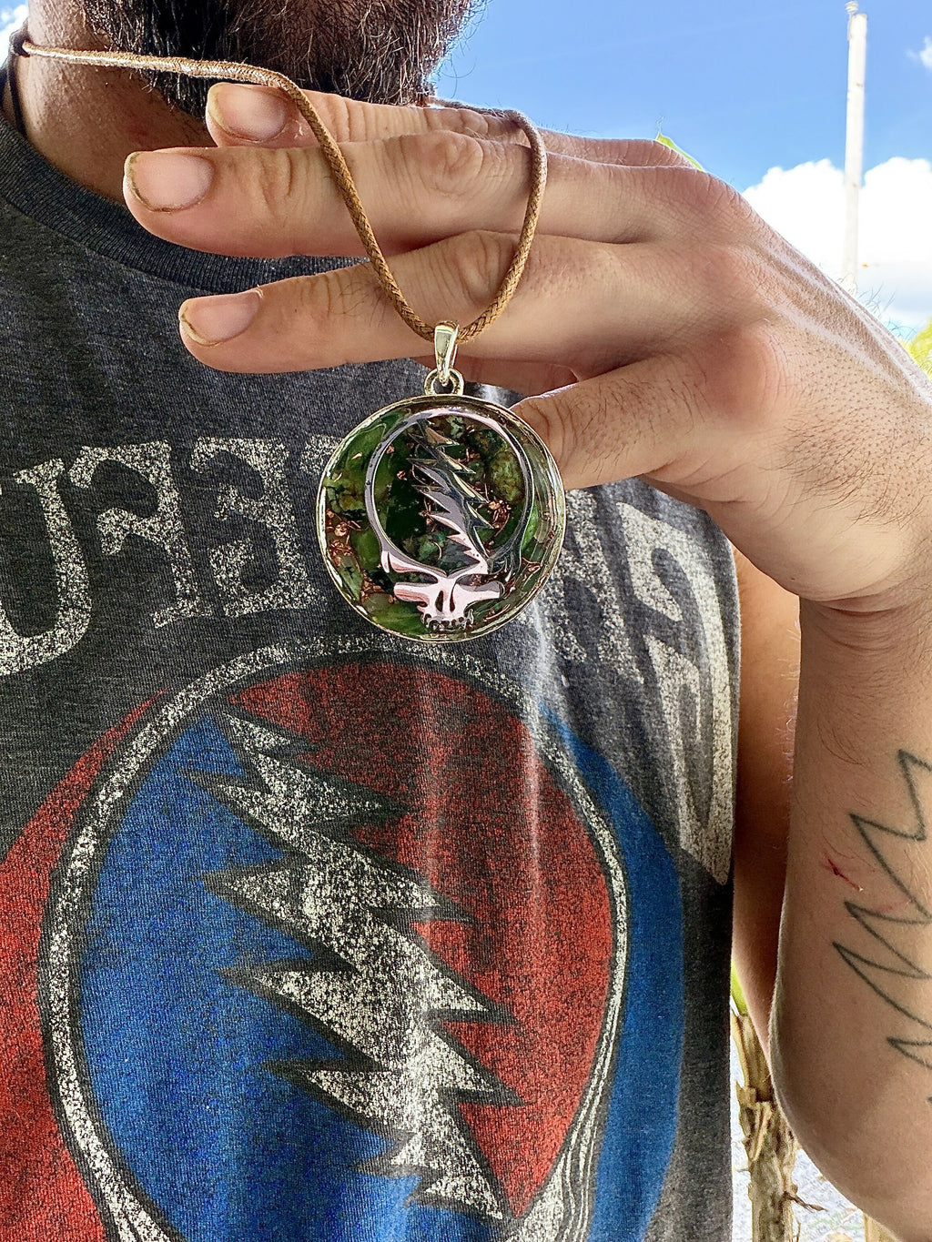 Pendant worn on a tan leather cord against a grey printed T-shirt