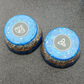 Two blue cupcake pieces with grey top discs showing a silver lotus and a triquetra, layered metal base visible