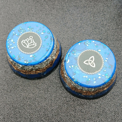 Two blue cupcake pieces with grey top discs showing a silver lotus and a triquetra, layered metal base visible