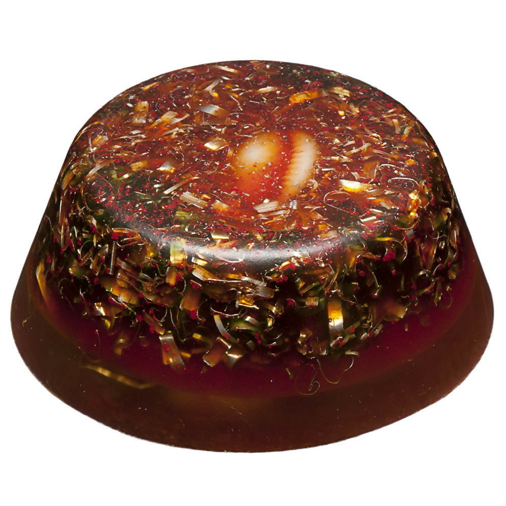Side view of the round brown piece with metal shavings and a cowrie shell on top