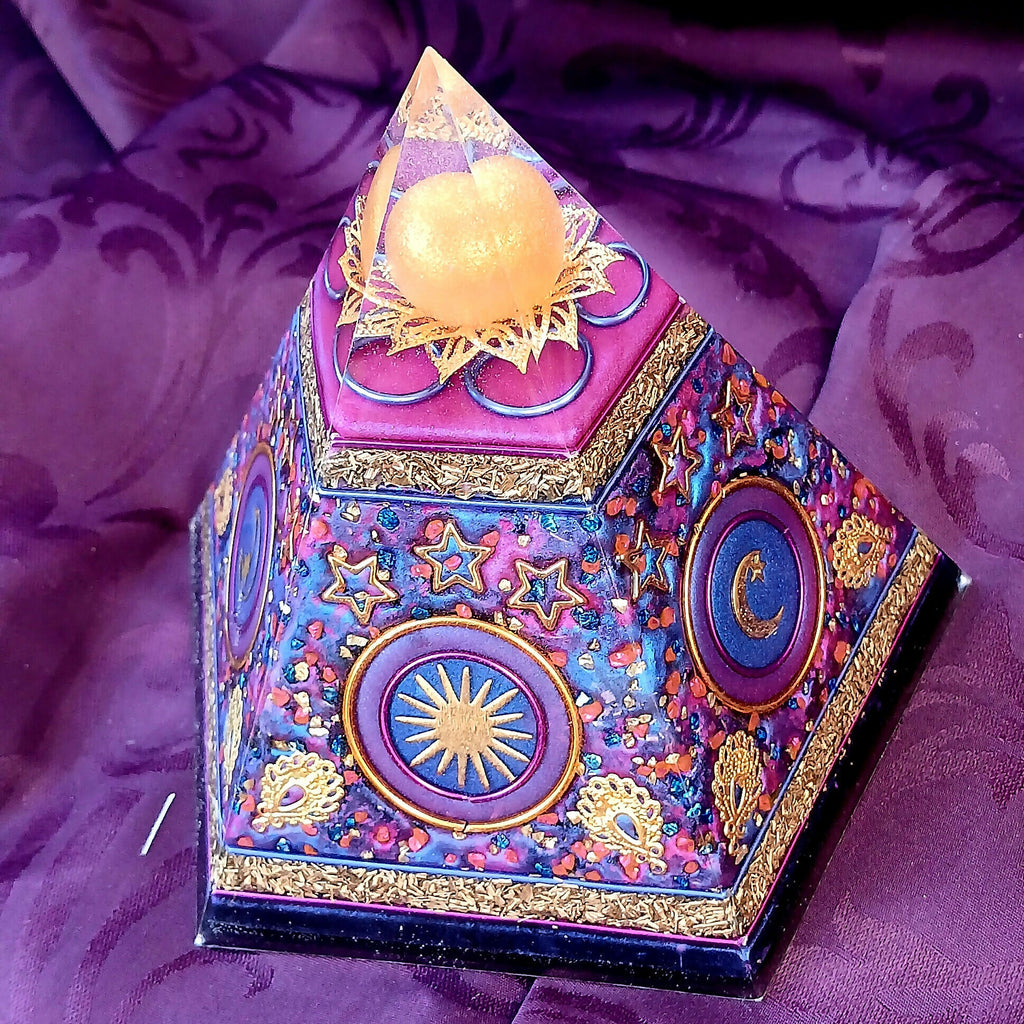 Angled view of blue and purple orgonite pyramid with sun, crescent moon and star decorations.