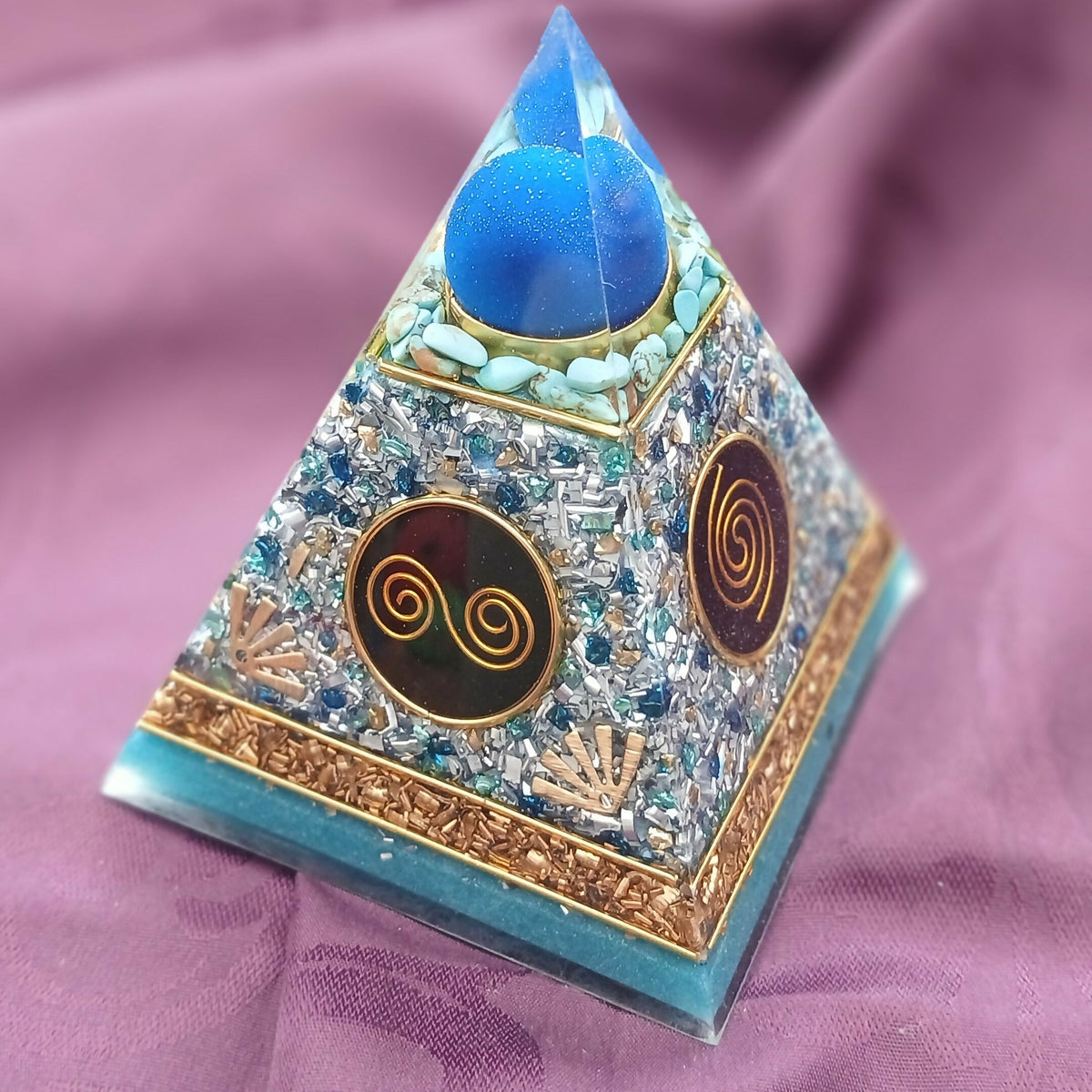 Front corner view showing the blue sphere, gold spiral discs and copper band above the turquoise base