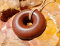 Red Rock Sedona Vortex Donut Pendant by Orgonite Andy – reddish-brown donut pendant on a tan cord, resting on orange and red layered rock