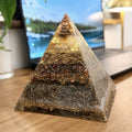 Abundance Orgonite Pyramid by Piezo & Co – layered pyramid with a golden top and copper coil tip on a wooden desk in front of a laptop