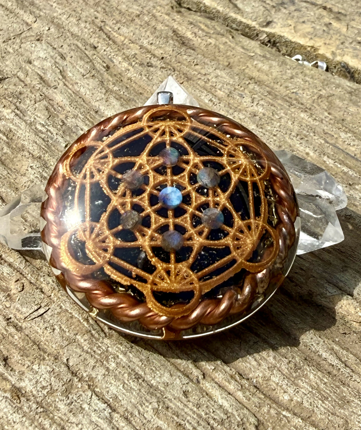 Front view of the pendant showing the copper-coloured Metatron’s Cube over a dark base with a blue stone at the centre, beside clear quartz points