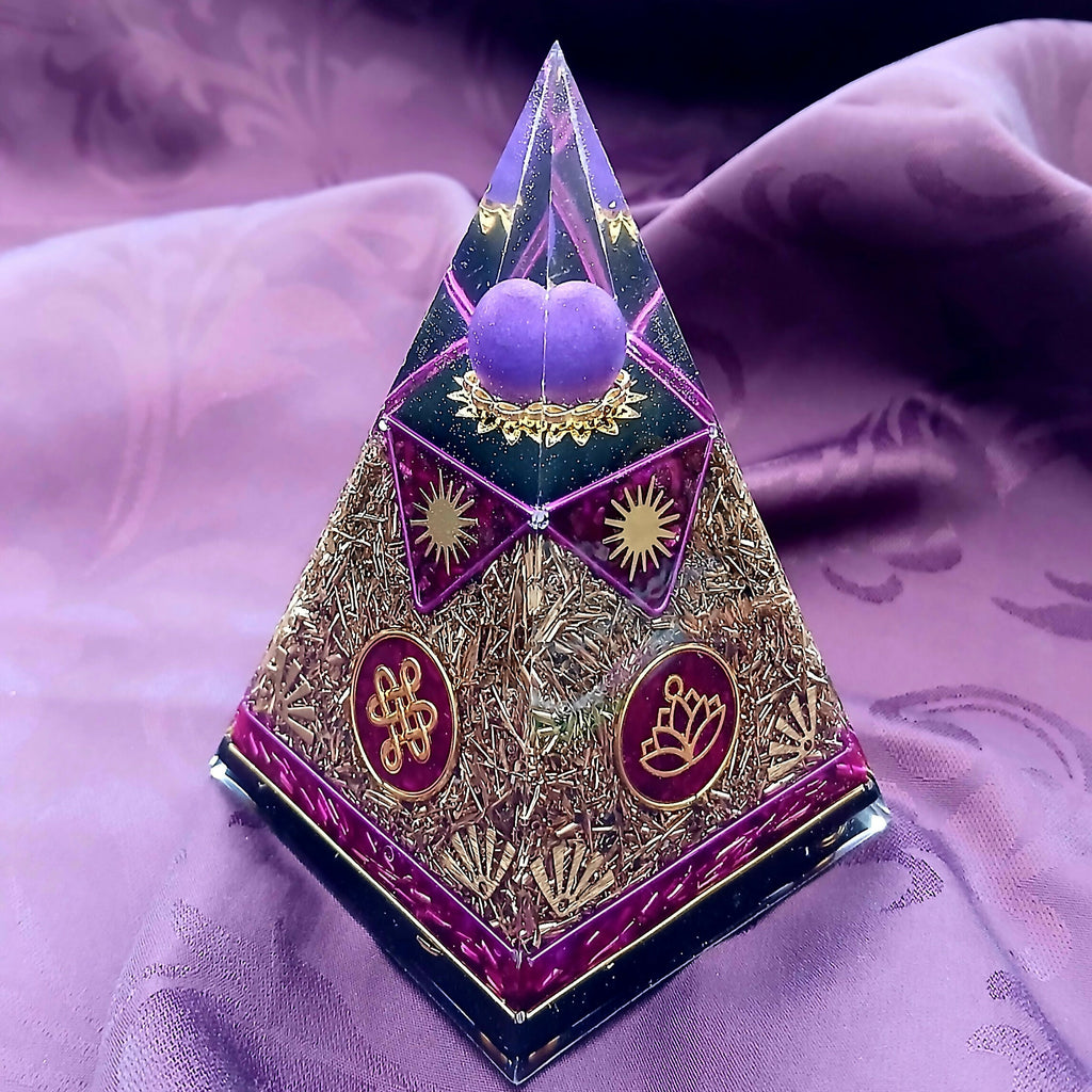 Small Nubian Pyramid by Orgone Art Yvonne – steep pyramid with a purple heart and sphere in the clear tip, gold flake panels, and red discs with gold knot and lotus symbols