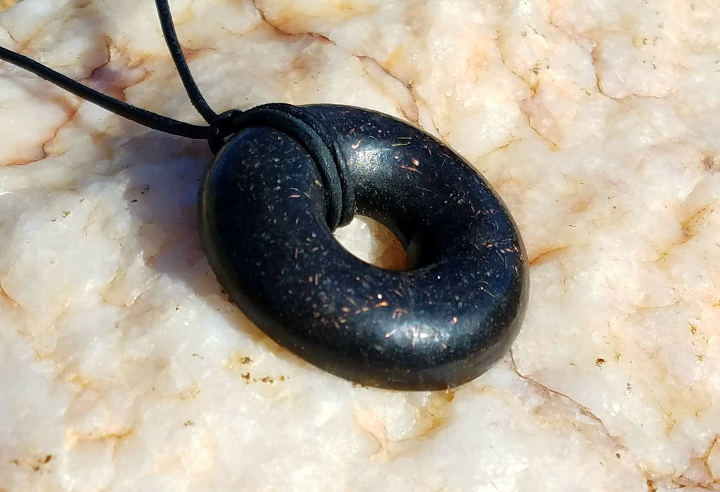 Angled close view of the black donut pendant and its cord lying on pale veined stone