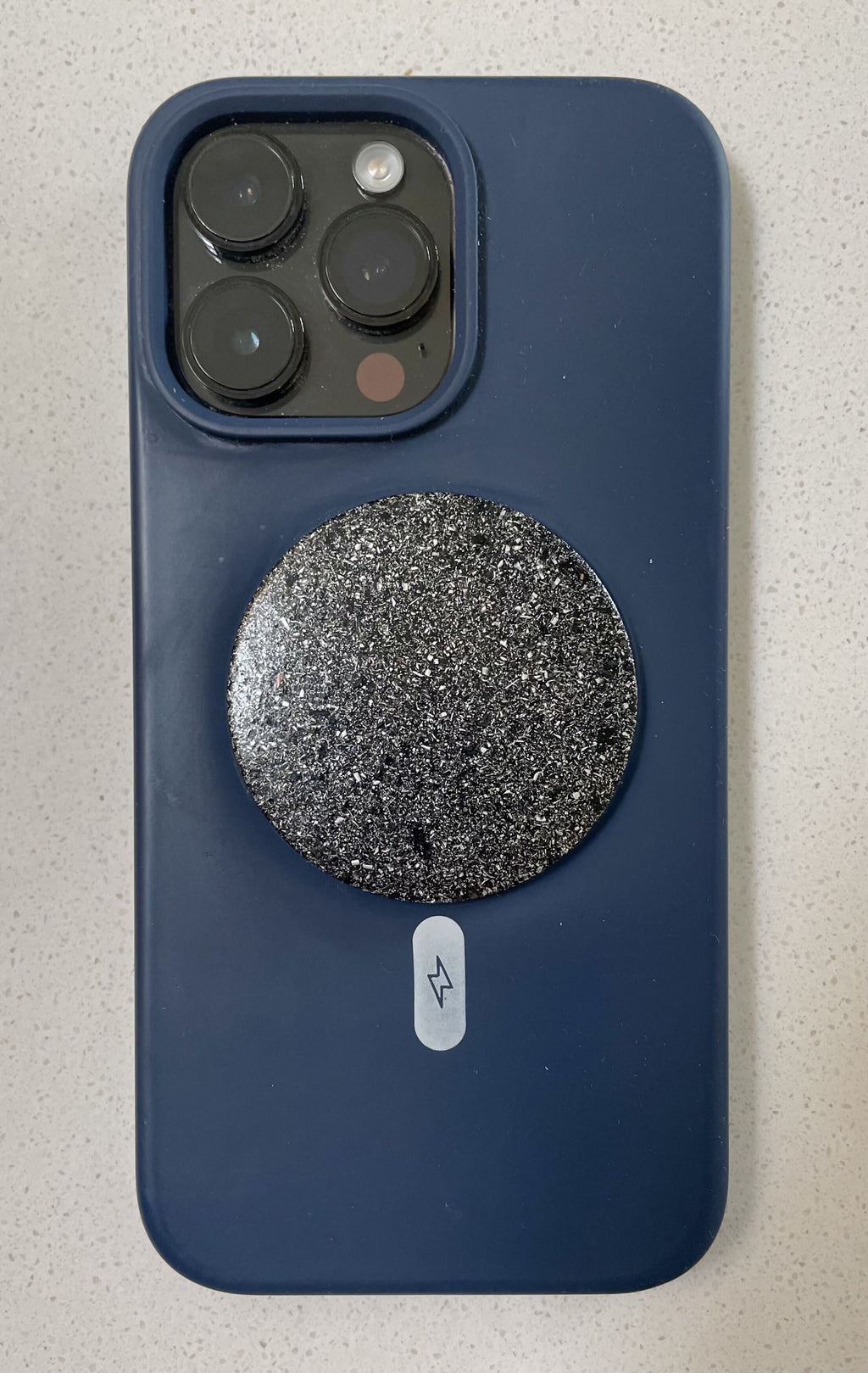 Round dark Maxishield disc attached to the back of a blue smartphone case