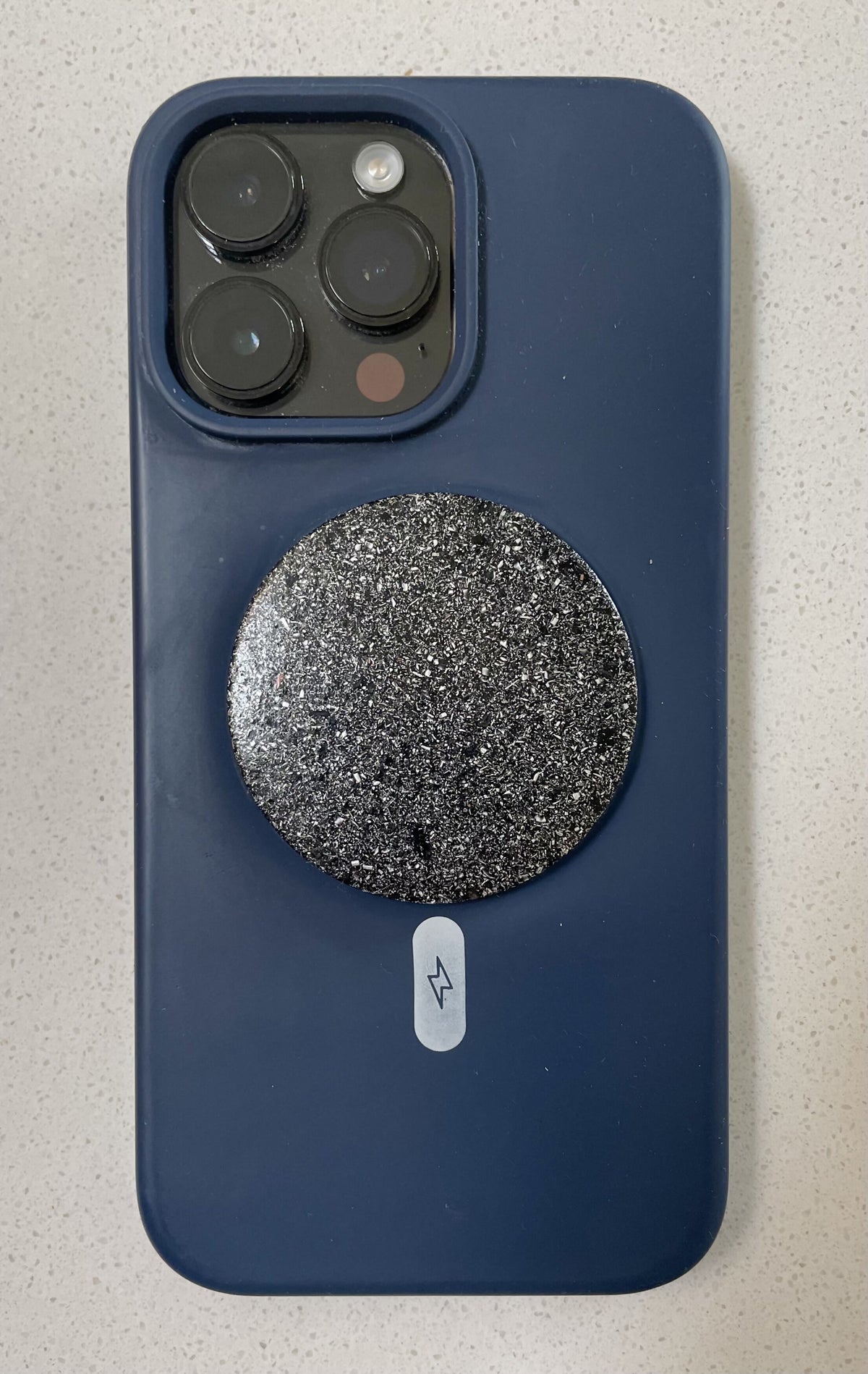 Round dark Maxishield disc attached to the back of a blue smartphone case