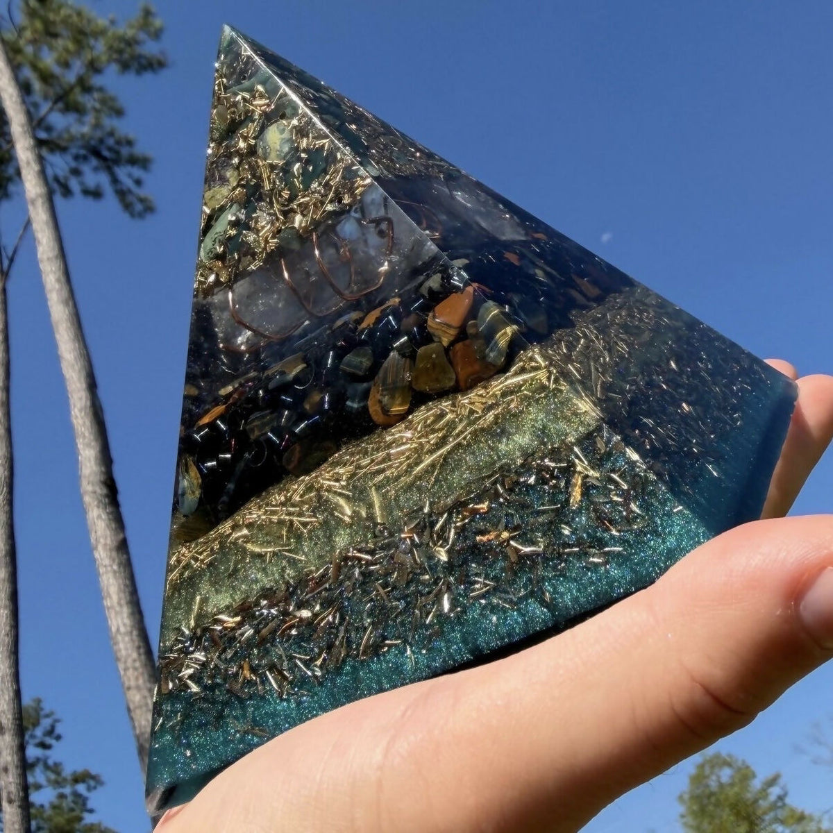 Bloodstone and Kambaba Jasper pyramid by Piezo & Co held in a hand against a blue sky, showing the stone, quartz and shaving layers close up
