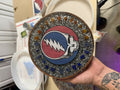 Stealie Lapis & Carnelian Charging Plate by Mark Ethan Designs – round plate with a red, white and blue skull and lightning-bolt design ringed by orange and blue stones and silver pieces, held in a hand