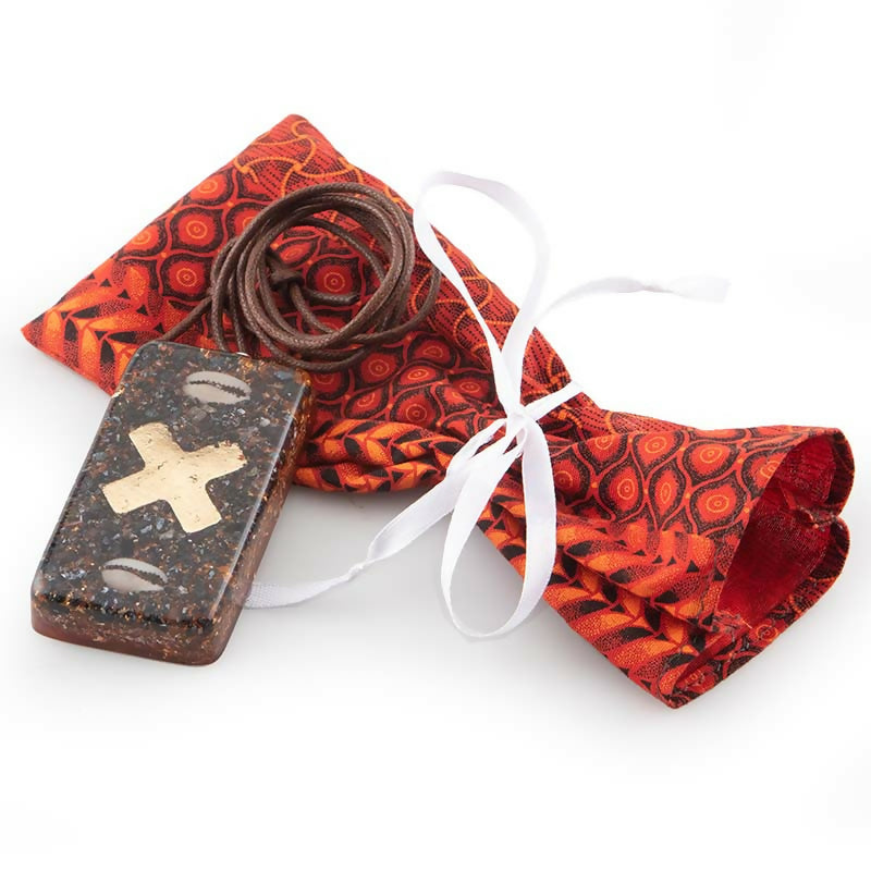 Brick with a gold cross and cowrie shells beside a red patterned fabric pouch, cord and white ribbon