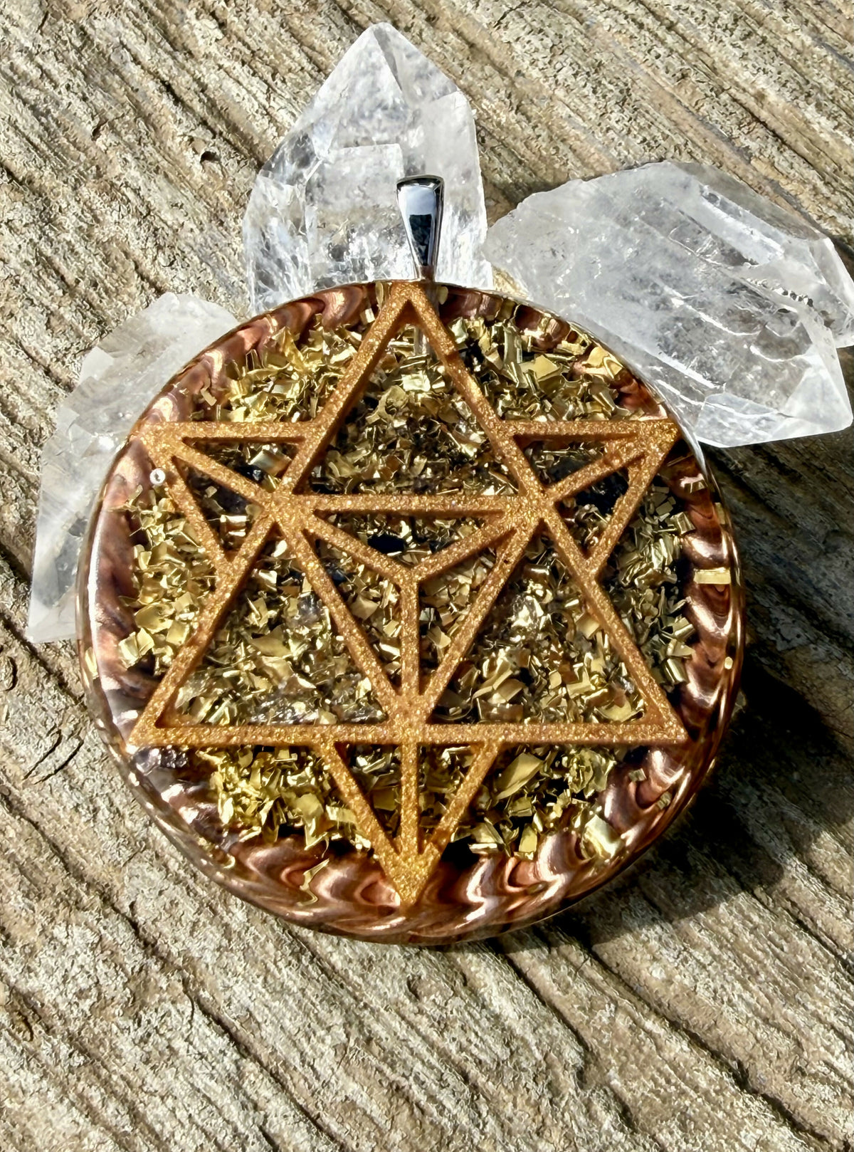 Pendant showing a copper-coloured star tetrahedron design over gold-coloured metal flakes, with twisted copper rim and clear quartz points behind