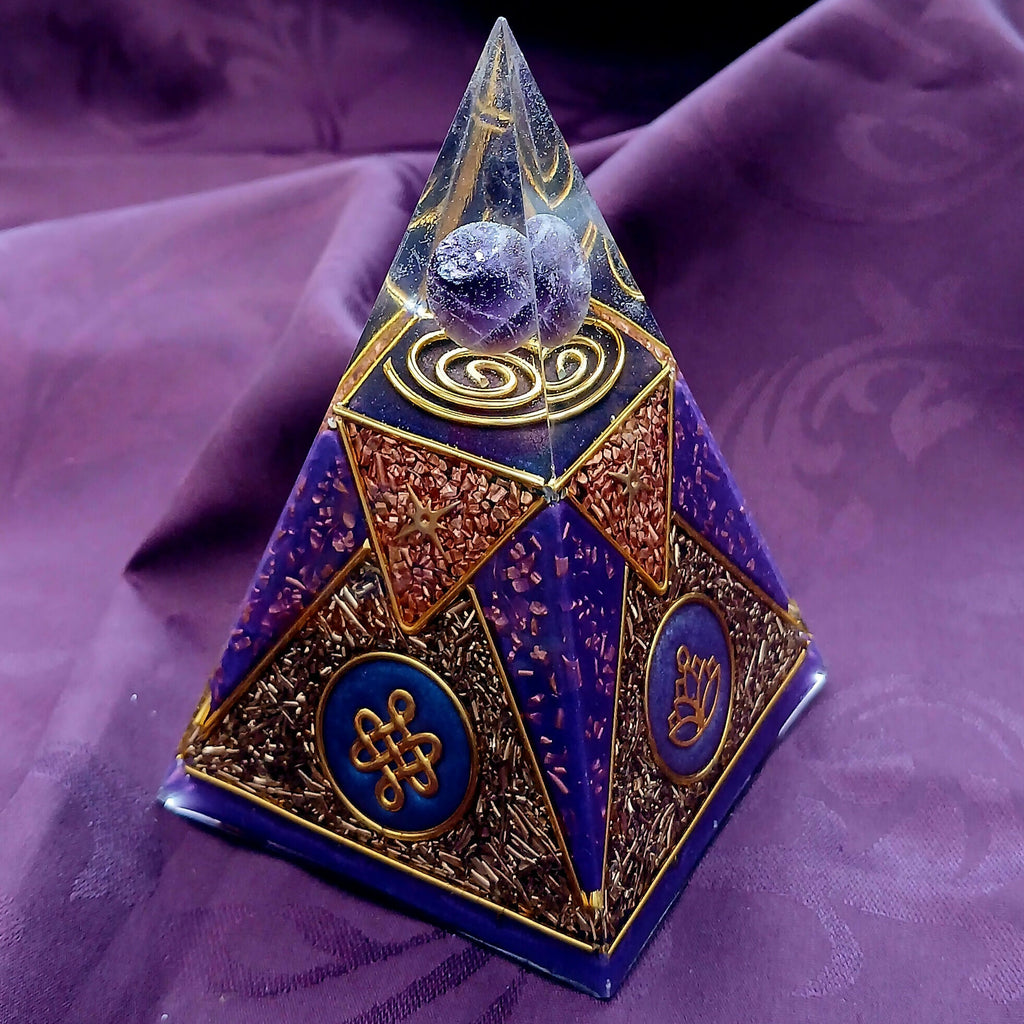 Small Purple Nubian Pyramid by Orgone Art Yvonne – tall purple and gold pyramid with a clear tip holding purple stones above a gold spiral, on purple fabric