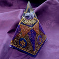 Small Purple Nubian Pyramid by Orgone Art Yvonne – tall purple and gold pyramid with a clear tip holding purple stones above a gold spiral, on purple fabric