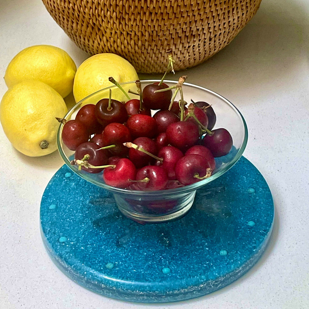 Plate in use under a glass bowl of cherries, beside lemons and a woven basket