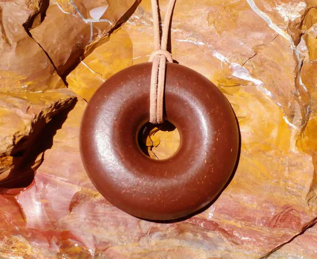Front view of the pendant and its looped tan cord on warm-coloured layered rock