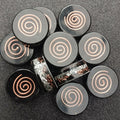 Close group of round black pocket discs, each with a raised copper spiral on top