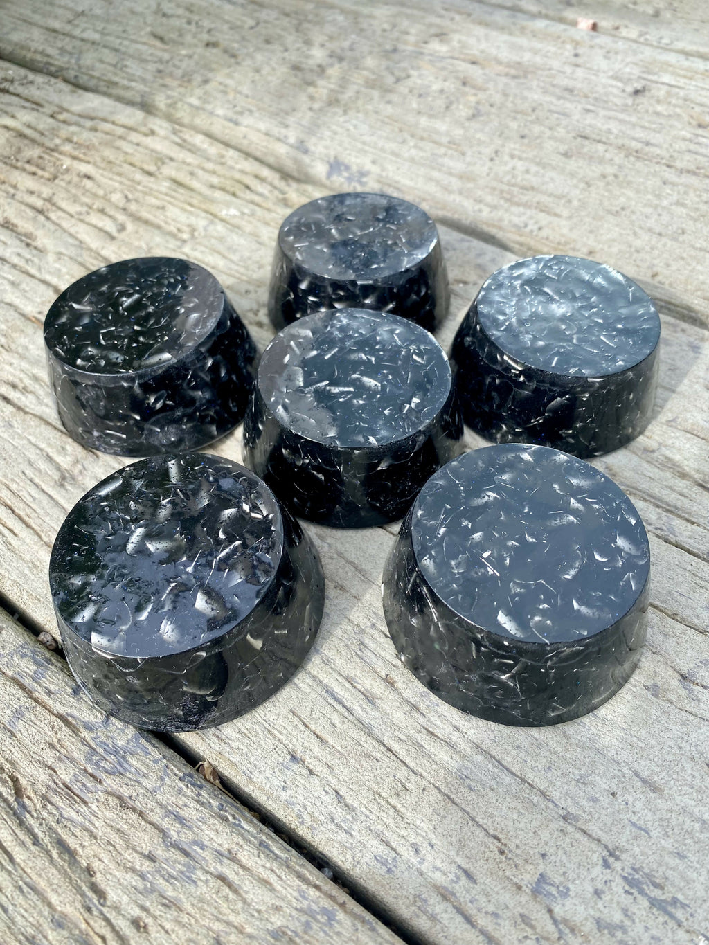 Six black shungite orgonite towerbusters grouped on a wooden surface, viewed from an angle