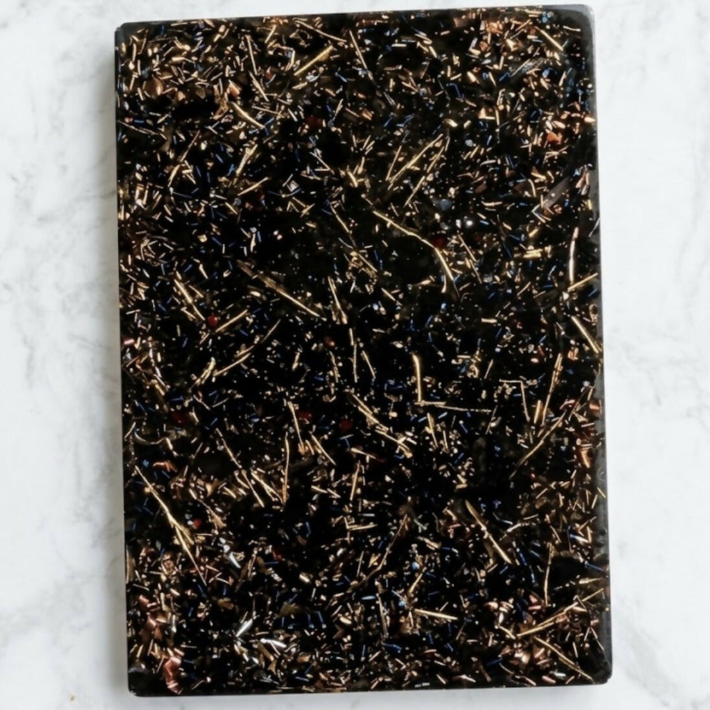Grounding Orgonite Charging Plate by Piezo & Co – rectangular black plate with gold-coloured metal shavings, top view on white marble