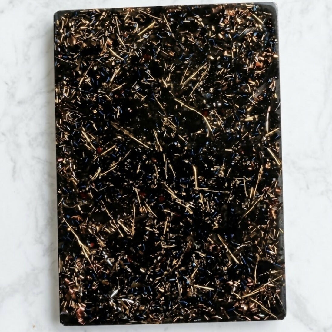 Grounding Orgonite Charging Plate by Piezo & Co – rectangular black plate with gold-coloured metal shavings, top view on white marble