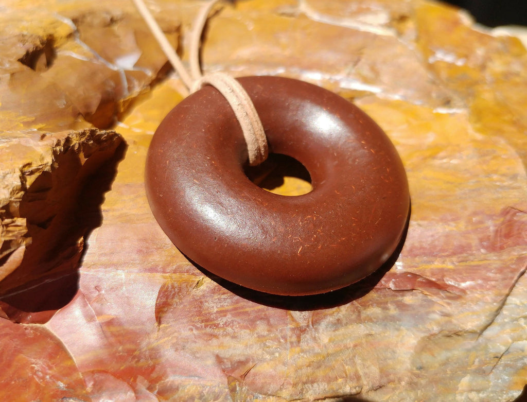 Angled view of the pendant on red and orange rock, showing its smooth rounded surface