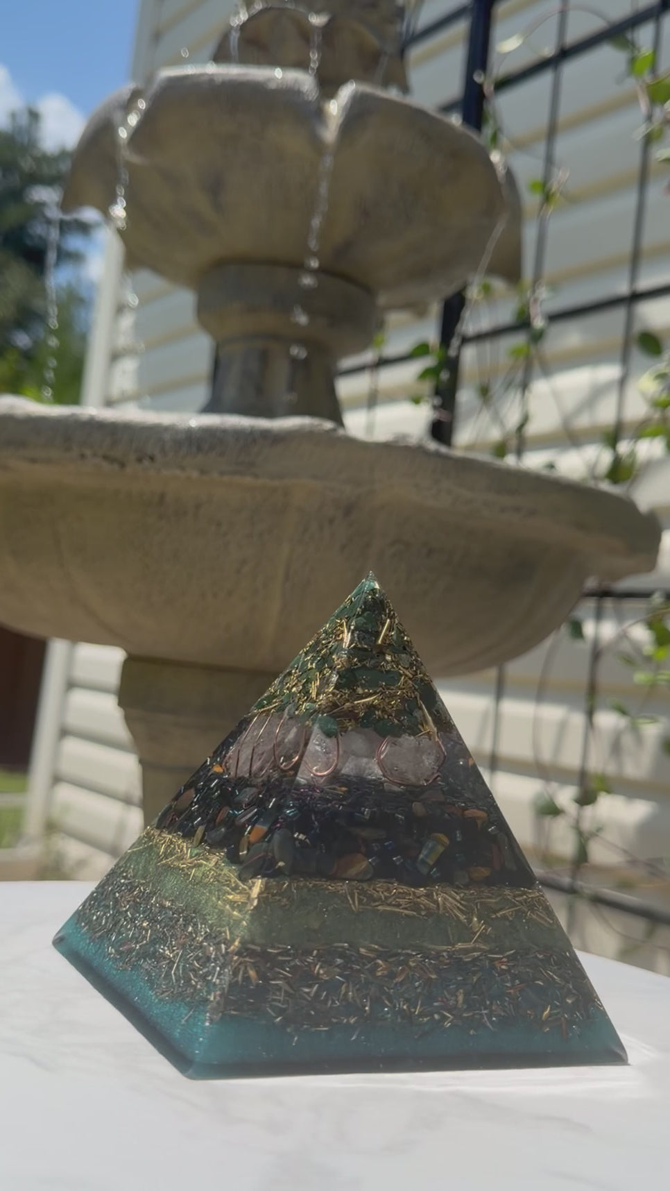 Short video of the Bloodstone and Kambaba Jasper pyramid by Piezo & Co on a white table in front of a stone fountain, filmed from the front as the camera moves slightly closer