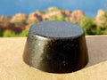 Large Black Sun Orgonite Tower Buster by Orgonite Andy – round black tower buster with a tapered side and glittery surface, on a ledge in front of red rock hills