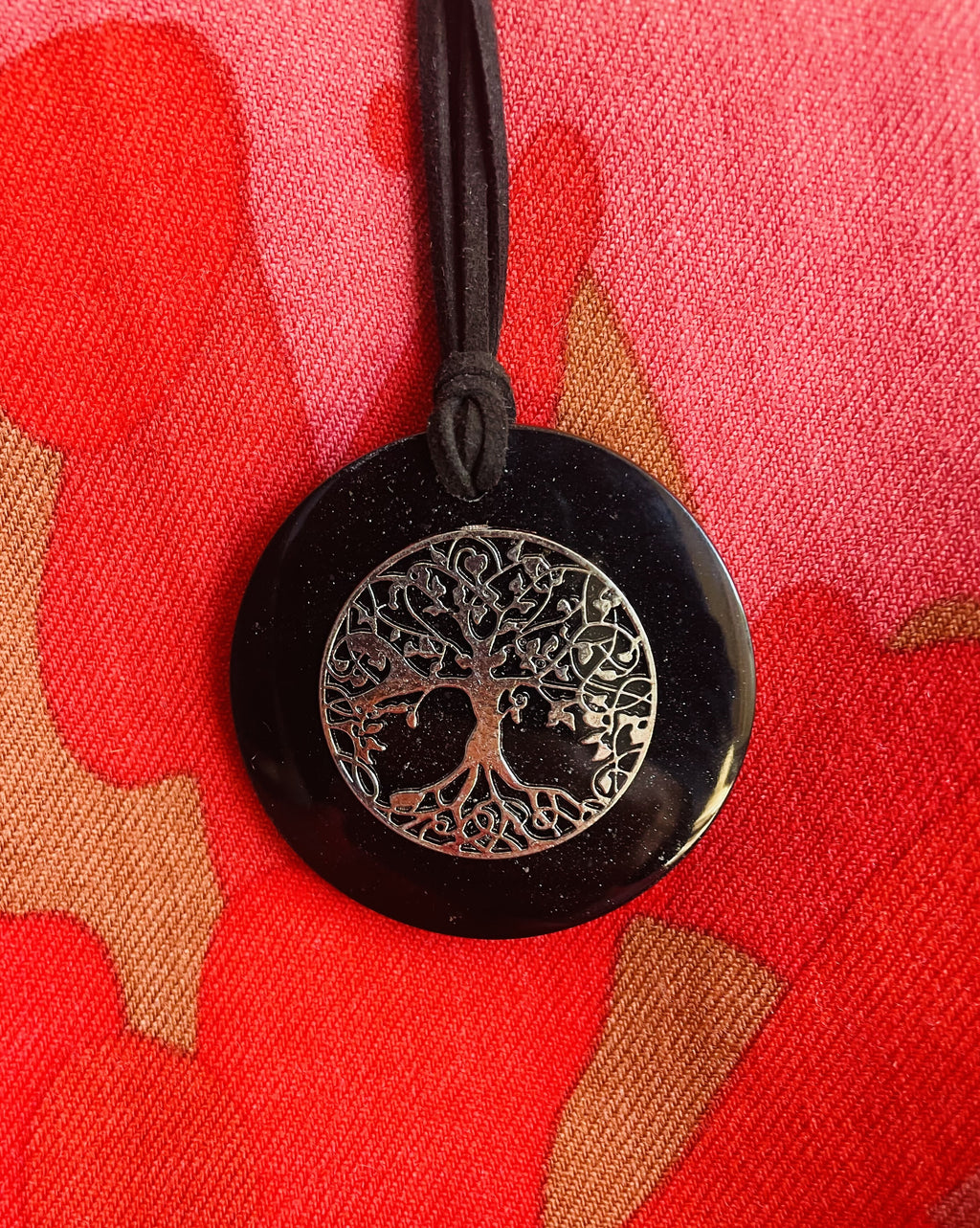 Black round tree-of-life pendant on its double black cord, shown against red clothing